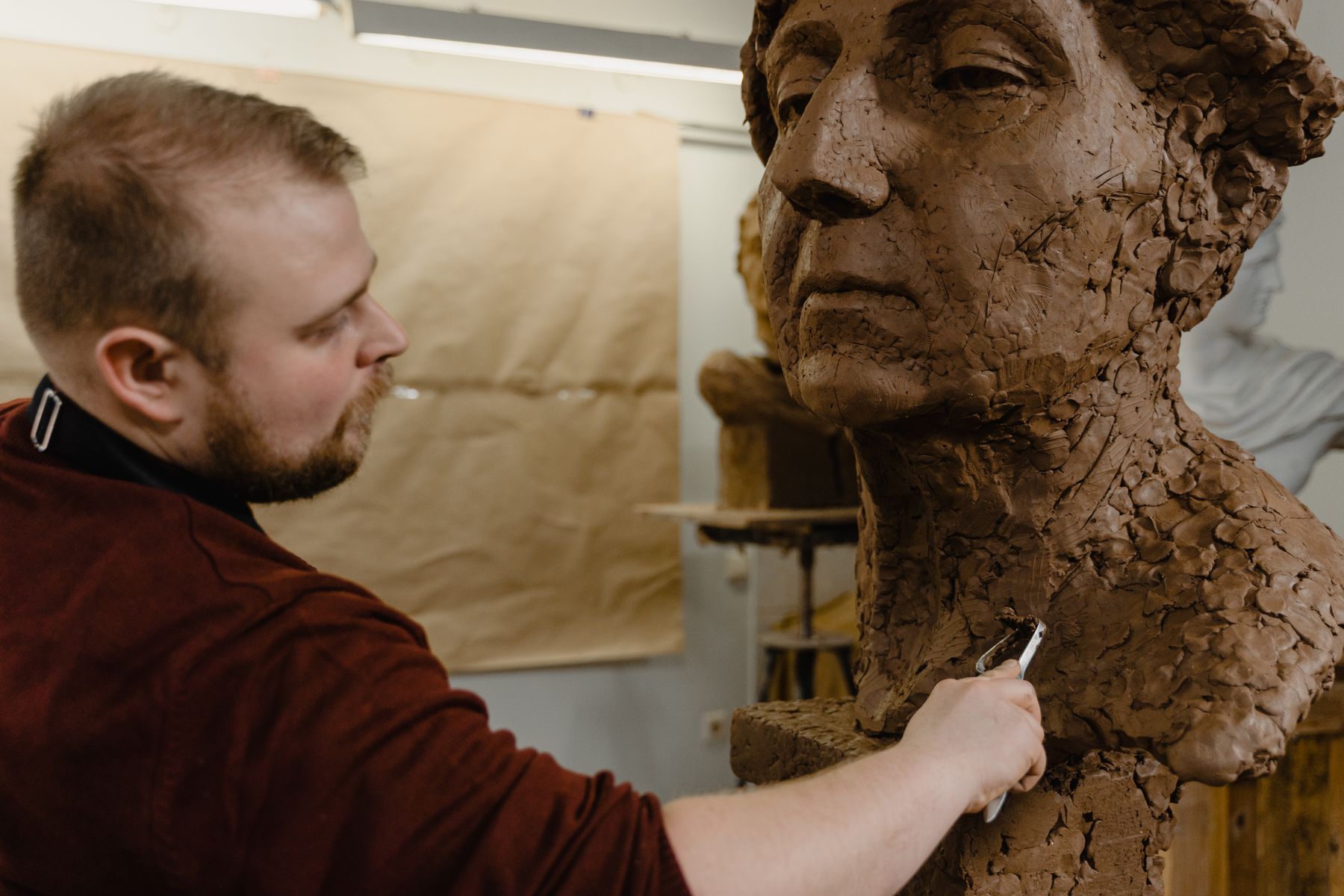 Sculptor refining the surface of a clay portrait with a loop tool