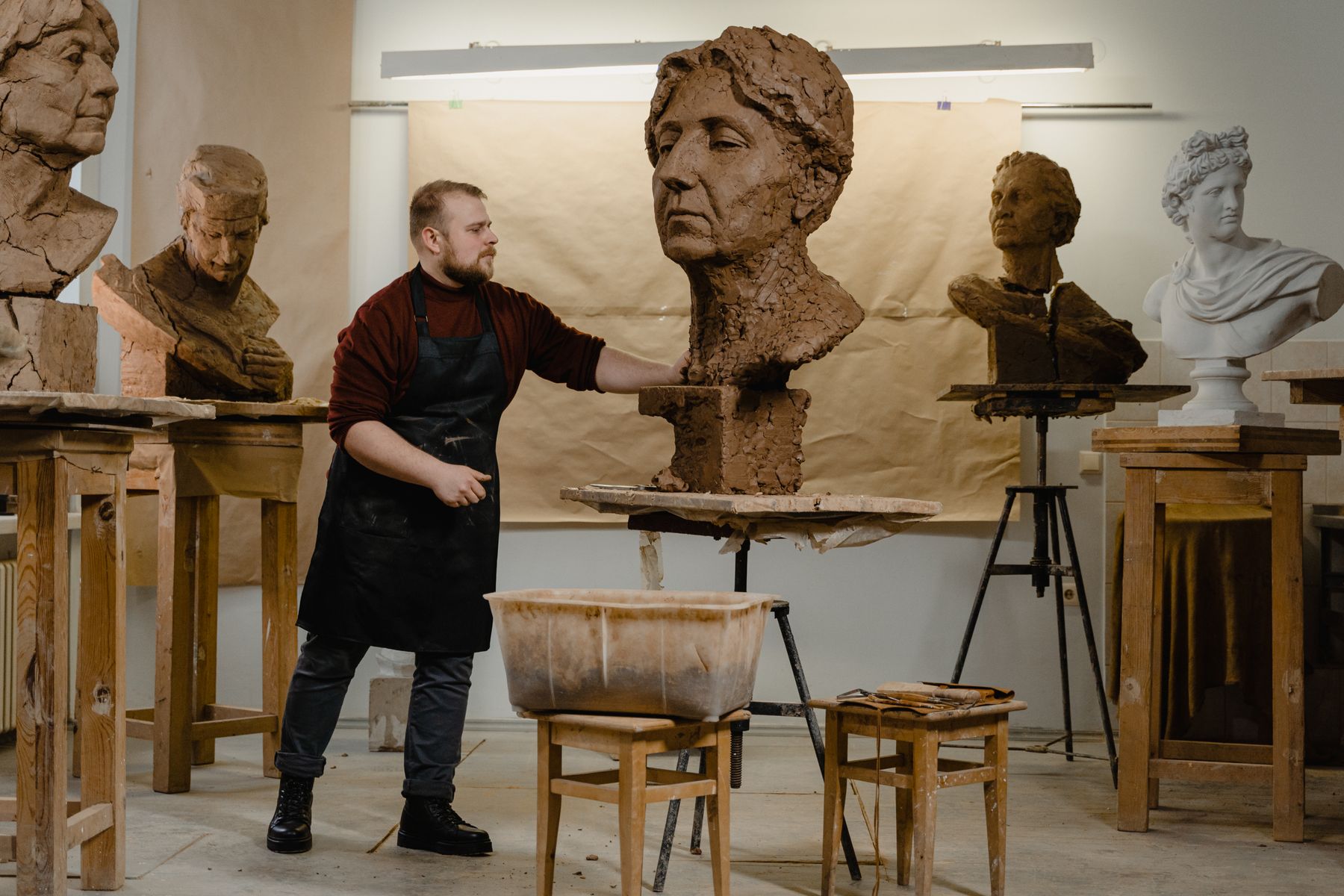 Sculptor standing among portrait studies while working on a monumental clay bust